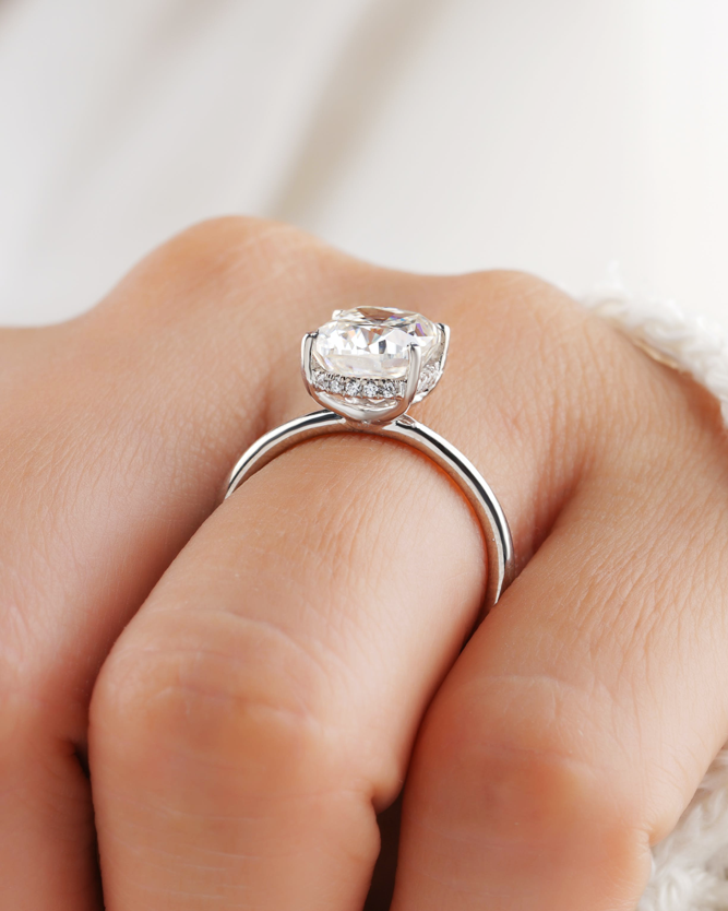 A close view of a cushion-cut engagement ring with a hidden halo on a slim plain band, worn on the hand