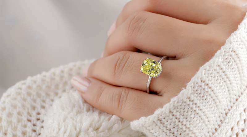 Large yellow cushion cut stone in white metal claws worn on a hand resting on a cream knitted sleeve