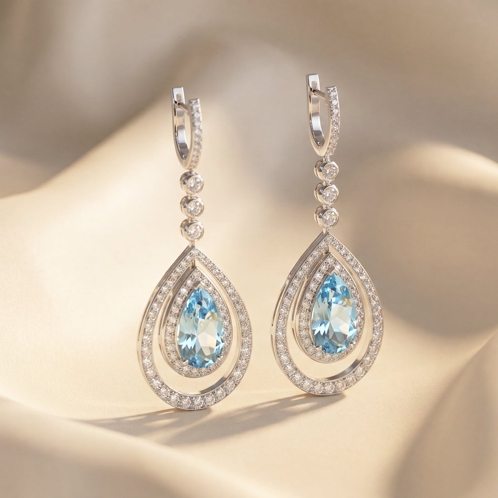 Pair of teardrop-shaped earrings with blue gemstones on a beige fabric background