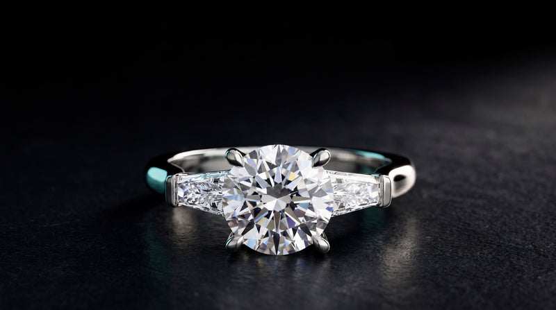 Three-stone engagement ring with baguette side stones, platinum, on a dark studio surface