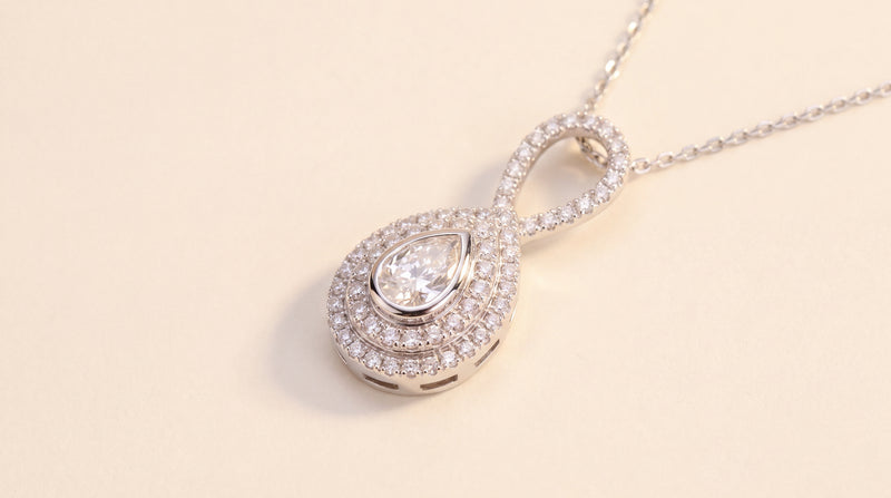A pear diamond pendant in a double halo with a diamond-set looped bail, on a fine chain