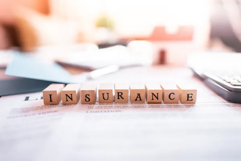 Wooden letter blocks spelling insurance on a printed document, pale keypad at the desk edge