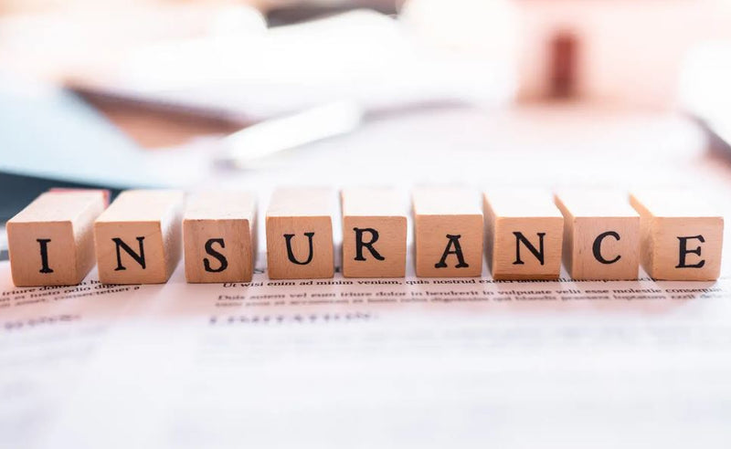 Close crop of wooden blocks reading insurance on paperwork, desk items blurred behind