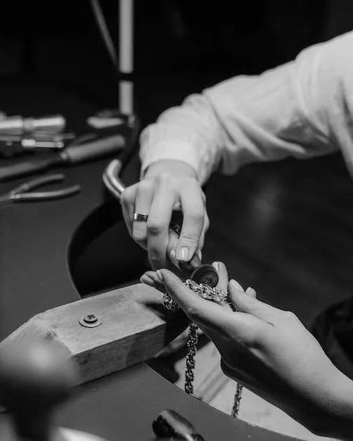 Hands over a wooden bench peg, holding a small dark tool above a silver coloured chain, black and white